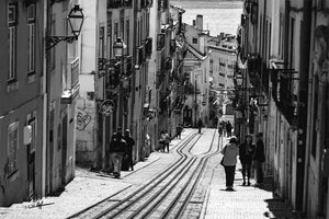 Black and white photo of a narrow city street with tram tracks and people walking.