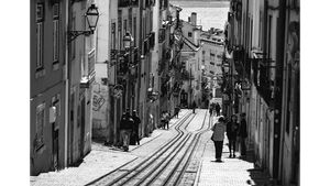 Black and white city street photo with tram tracks, people walking, and historic buildings.