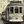 Vintage tram on narrow city street with Monkey 47 advertisement, people walking nearby
