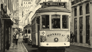 Vintage tram on narrow city street with Monkey 47 advertisement, people walking nearby