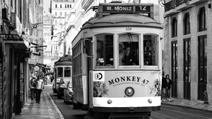 Black and white photo of vintage Lisbon tram on narrow city street with people walking