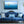 Elegant living room with blue tufted sofa, decorative pillows, and wall art of a boat at sea