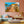 Modern living room with pastel decor, featuring a large wall art of a tropical pier and boats.
