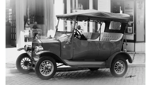 Monochrome photo of a vintage convertible car parked on a cobblestone street.