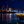Night view of illuminated port with cranes, starry sky, and lively waterfront dining terrace over water.