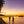 Tropical beach sunset with palm trees, people, pier, and boats on calm ocean water