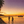 Tropical beach sunset with palm trees, people on the shore, boats, and a wooden pier
