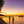 Tropical beach sunset with palm trees, people by the shore, boats and a pier over the ocean