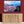 Framed cityscape wall art above wooden cabinet against red wall, with potted snake plant