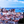 Panoramic view of city with red rooftops by a river and distant ship under blue sky