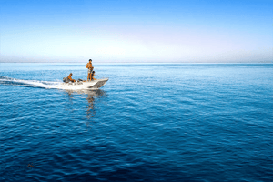 Three people on a small boat crossing calm blue sea under a clear sky, fine art photography