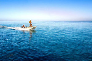 Three people on a small motorboat riding across calm blue ocean under clear sky