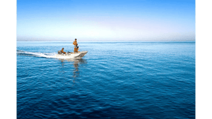 Three people riding a small motorboat on calm blue ocean under clear sky