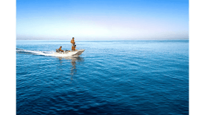 Three people riding a small motorboat on calm blue ocean under a clear sky