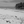 Black and white photo of a deserted tropical beach with driftwood, palm trees, and a lone figure by the shore.