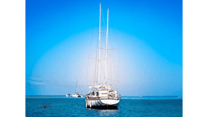 White sailboat anchored on calm blue sea with clear sky and distant boats