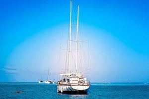 Sailboat anchored on calm blue sea with clear sky, other boats in distant background