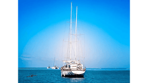 Sailboat anchored on calm blue sea under clear sky, with other boats in the background