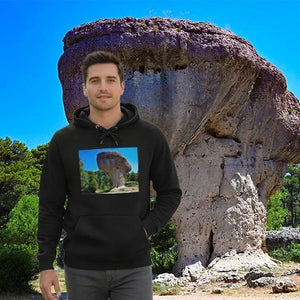 Man wearing black hoodie with rock formation print, standing in front of the same rock formation outdoors