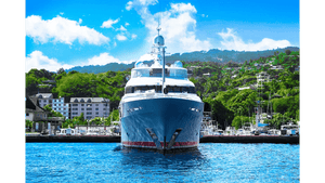 Luxury yacht docked at marina with lush green hillside and blue sky in background