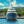 Large yacht docked at marina with blue sky and lush hillside in the background