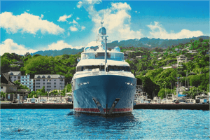 Large yacht docked at marina with blue sky and lush hillside in the background