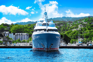 Luxury yacht docked at marina with hills and buildings in background, blue sky above