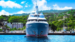 Luxury yacht docked at marina with lush green hillside and blue sky in background
