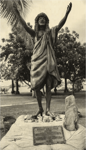Bronze Polynesian statue with arms raised, traditional attire, outdoor park setting, Tahiti