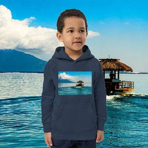 Child wearing blue eco-friendly hoodie with tropical boat print, standing by water