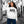 Woman wearing a white eco-friendly hoodie with a streetcar graphic, posing on a city street.