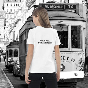 Child wearing white organic cotton t-shirt with 'I love you, Dad and Mom!' text, standing in front of a vintage tram in a city street.