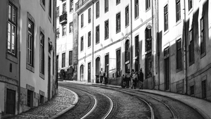 Black and white photo of curved urban street with tram tracks and people by historic buildings