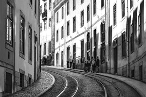Black and white urban street photo with tram tracks, old buildings, and people walking