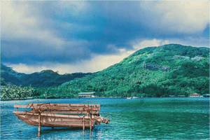 Wooden boat with paddle wheels on blue water, green lush island and mountains in background