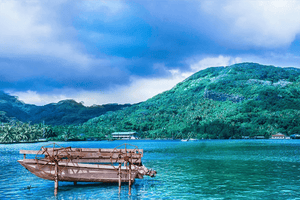 Colorful landscape with green island, paddle boat on blue water, dramatic clouds
