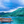 Rustic wooden raft on turquoise water with lush green island and cloudy sky background