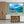 Modern kitchen with wall art of a scenic boat on blue water and lush green island landscape.