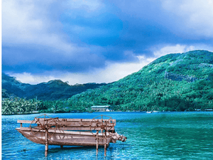 Wooden pedal boat on serene blue water with lush green island and cloudy sky